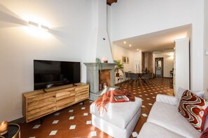 A living room with a TV, a fireplace, a dining area, and a kitchen in the background. - Apartments Florence -Faenza Terrace (Florence)