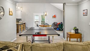 Een woonkamer met een tafeltennistafel, een bank en een klein houten bijzettafeltje met een plant.