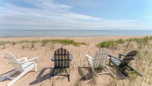 Three Adirondack chairs on a sandy beach with a view of the ocean.