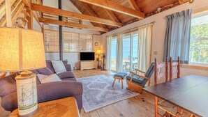 A cozy living room with a wooden ceiling, a sofa, a coffee table, a TV, and a dining area with a table and chairs.