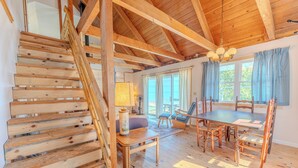 A wooden staircase leading to a dining area with a table and chairs, a lamp, and a window with curtains.