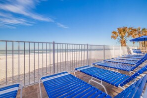 Un espace de détente aménagé sur la plage, avec des chaises longues bleues et une clôture blanche d’où l’on peut admirer l’océan.