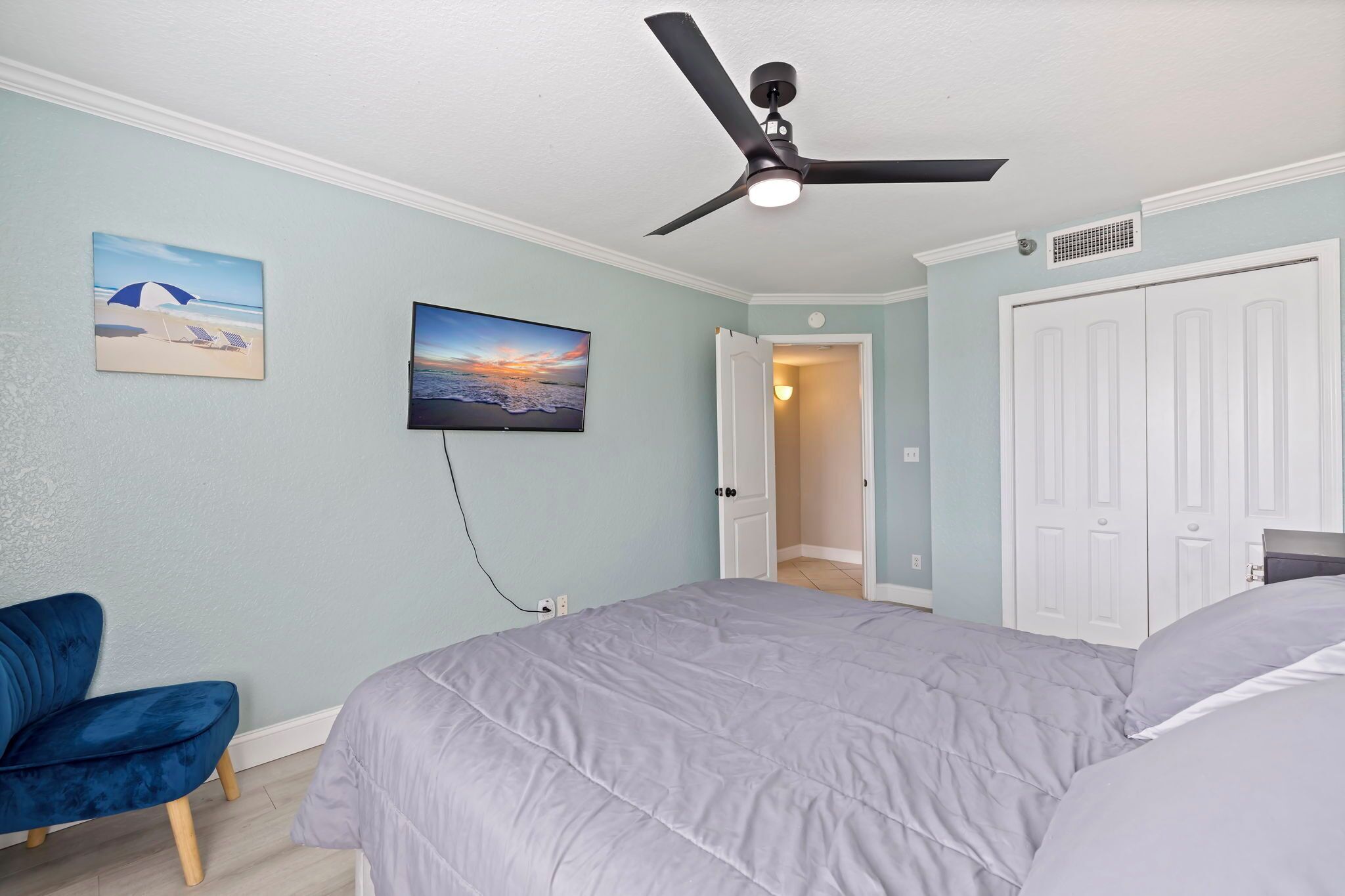 A bedroom with a bed, a ceiling fan, a TV, and a door leading to another room.