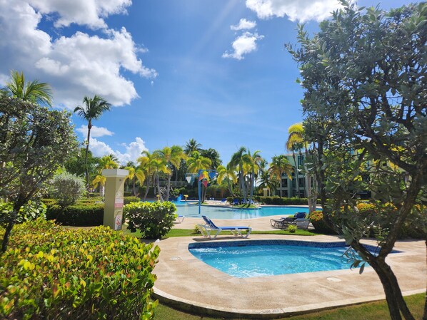 Zona de piscina con sillas de descanso, palmeras y un cielo azul despejado.