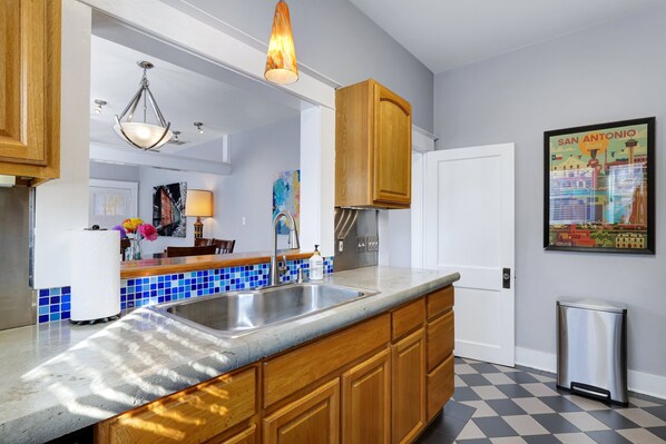 A kitchen with wooden cabinets, a stainless steel sink, and a tiled backsplash. - Mosaic - A Birdy Vacation Rental (San Antonio)