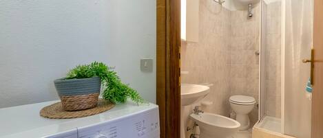 A compact bathroom with a washing machine, a bidet, a toilet, and a shower area.