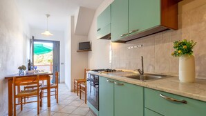 A kitchen with green cabinets, a tiled backsplash, a sink, and a dining area with chairs and a table.