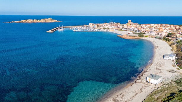 An aerial view of a coastal town with a marina, sandy beach, and historic buildings.