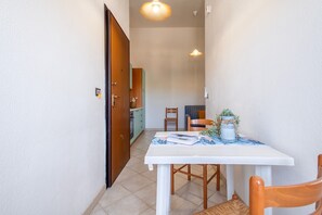 A narrow hallway with a dining table and chairs, a wooden door, and a kitchen area in the background.