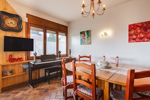 Un comedor con una mesa de madera, sillas, un piano, un televisor y obras de arte en las paredes.