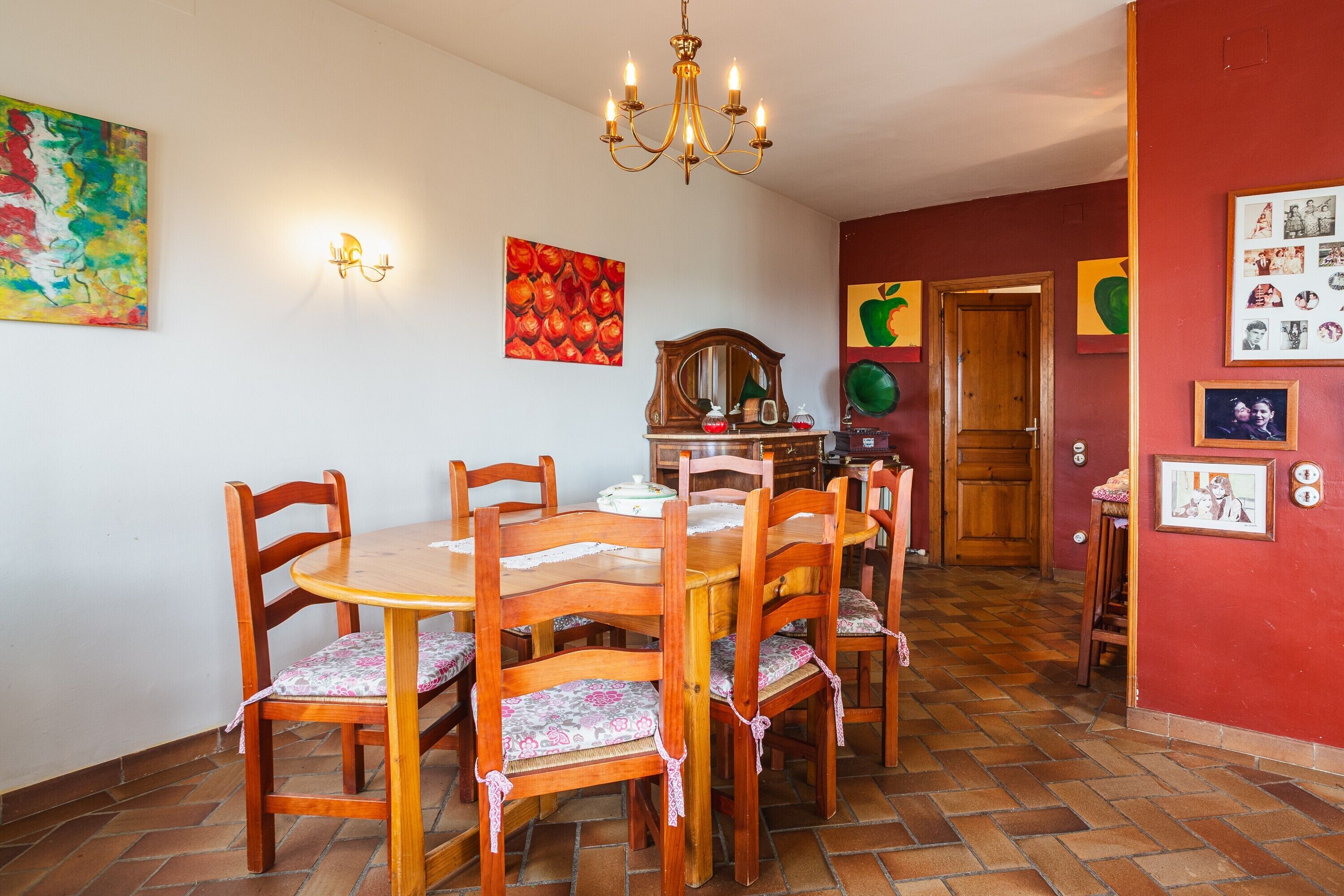 Un comedor con mesa y sillas de madera, una araña y obras de arte en la pared.