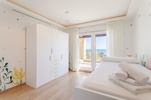 Une chambre avec un lit, une armoire, une porte-fenêtre coulissante donnant sur un balcon et une vue sur la mer.