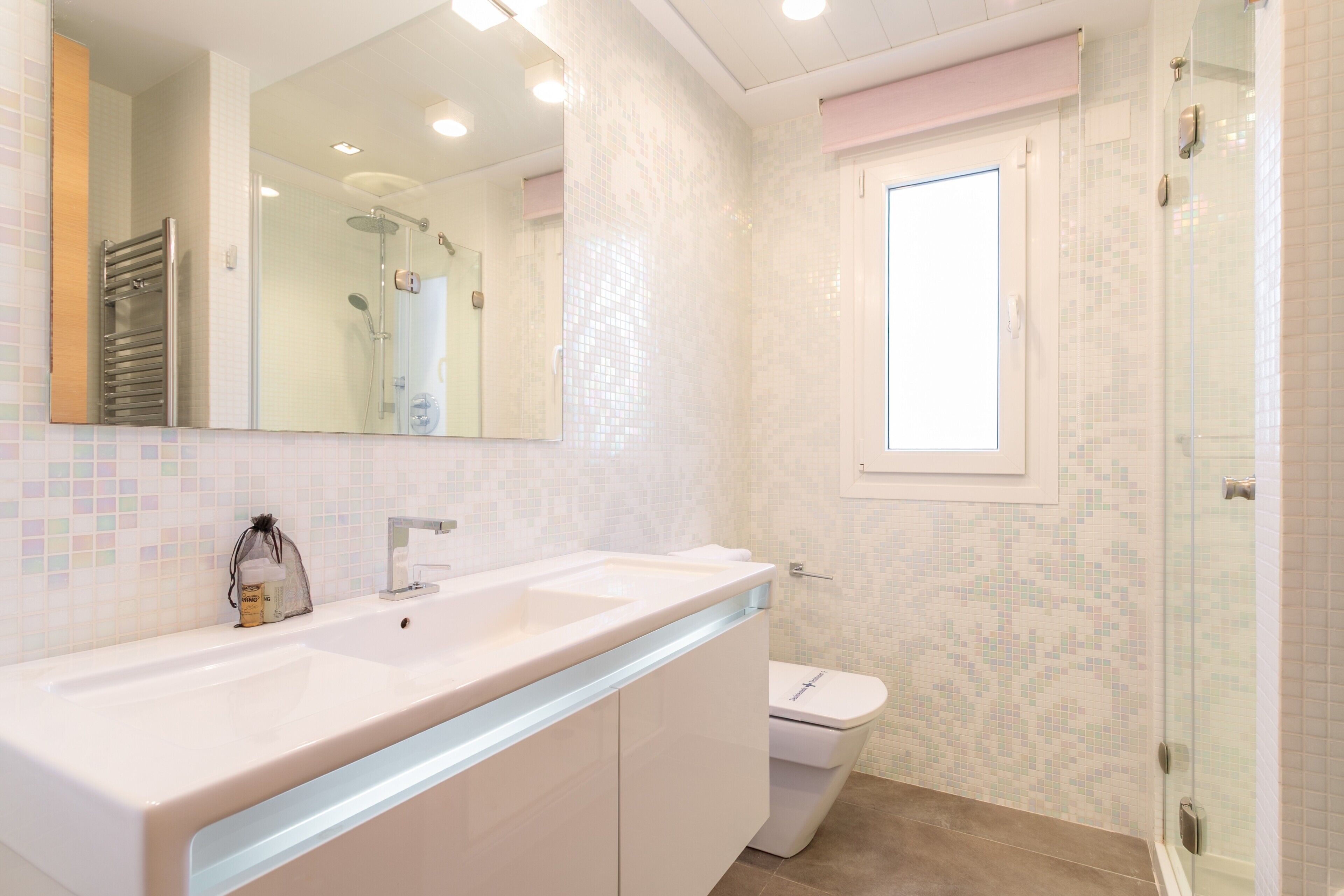 Un baño con un espejo grande, un lavamanos, un inodoro y una zona de ducha.