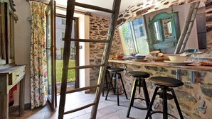 A rustic kitchen with a stone wall, wooden ladder, and bar stools. - Casetta 'Delle Castagne' with Mountain View, Wi-Fi, and Air Conditioning (Casaleggio Boiro)