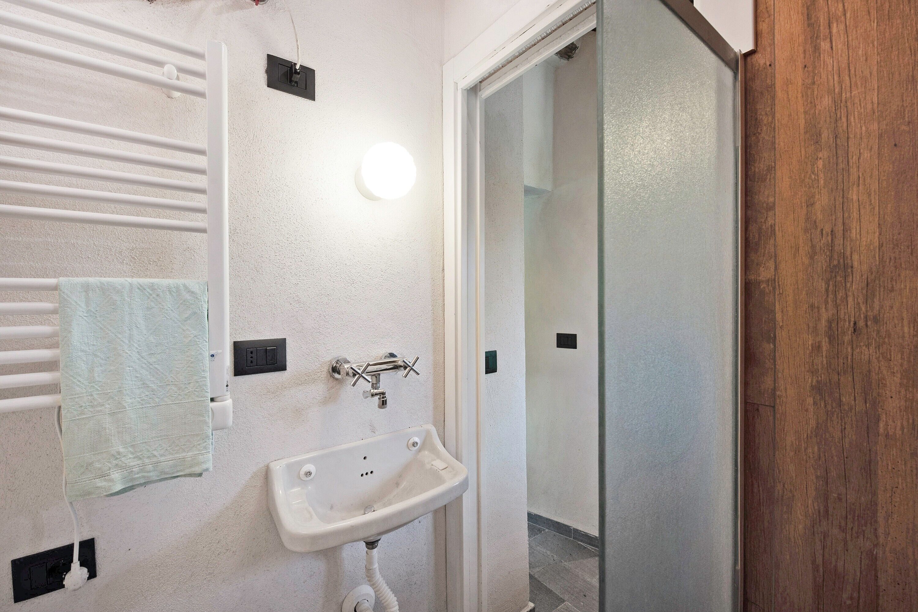 A bathroom with a white sink, a towel rack, a light fixture, and a wooden door.