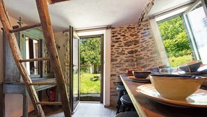 A kitchen with a wooden ladder, a stone wall, and a view of the garden through an open door. - Casetta 'Delle Castagne' with Mountain View, Wi-Fi, and Air Conditioning (Casaleggio Boiro)