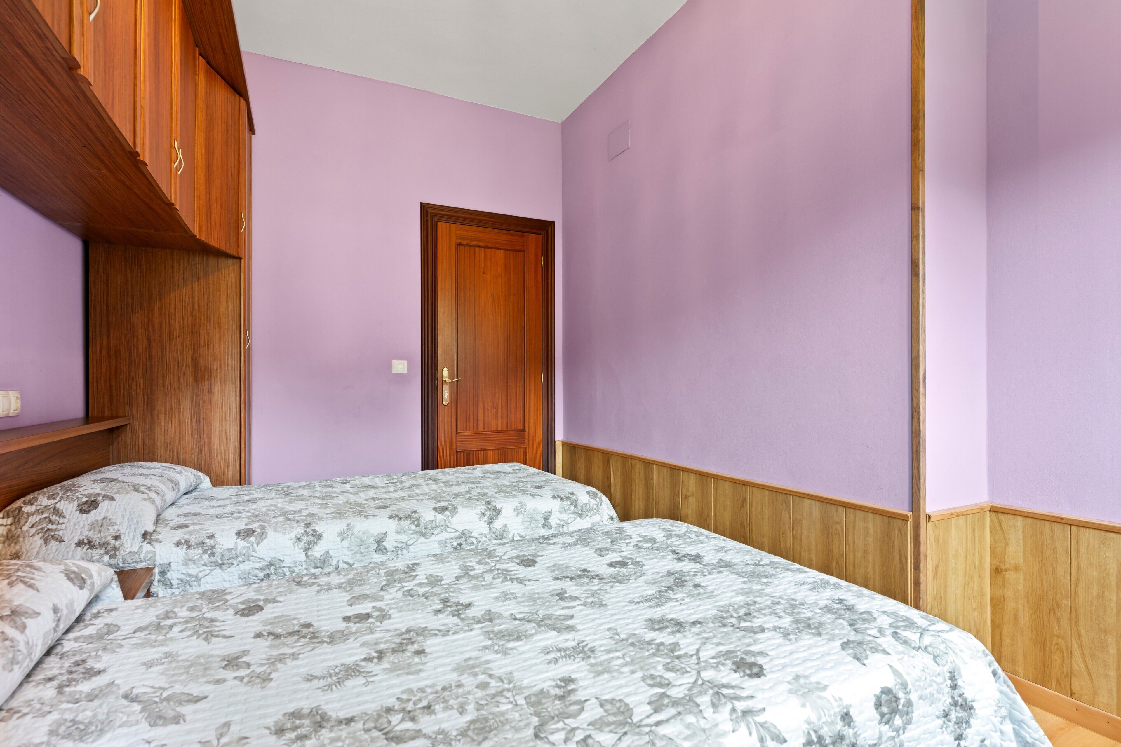 Un dormitorio con armario de madera, una puerta y una cama con ropa de cama floral.
