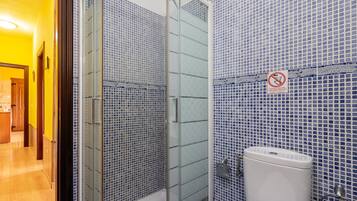 Een badkamer met blauwe mozaïektegels, een glazen douchecabine en een toilet.