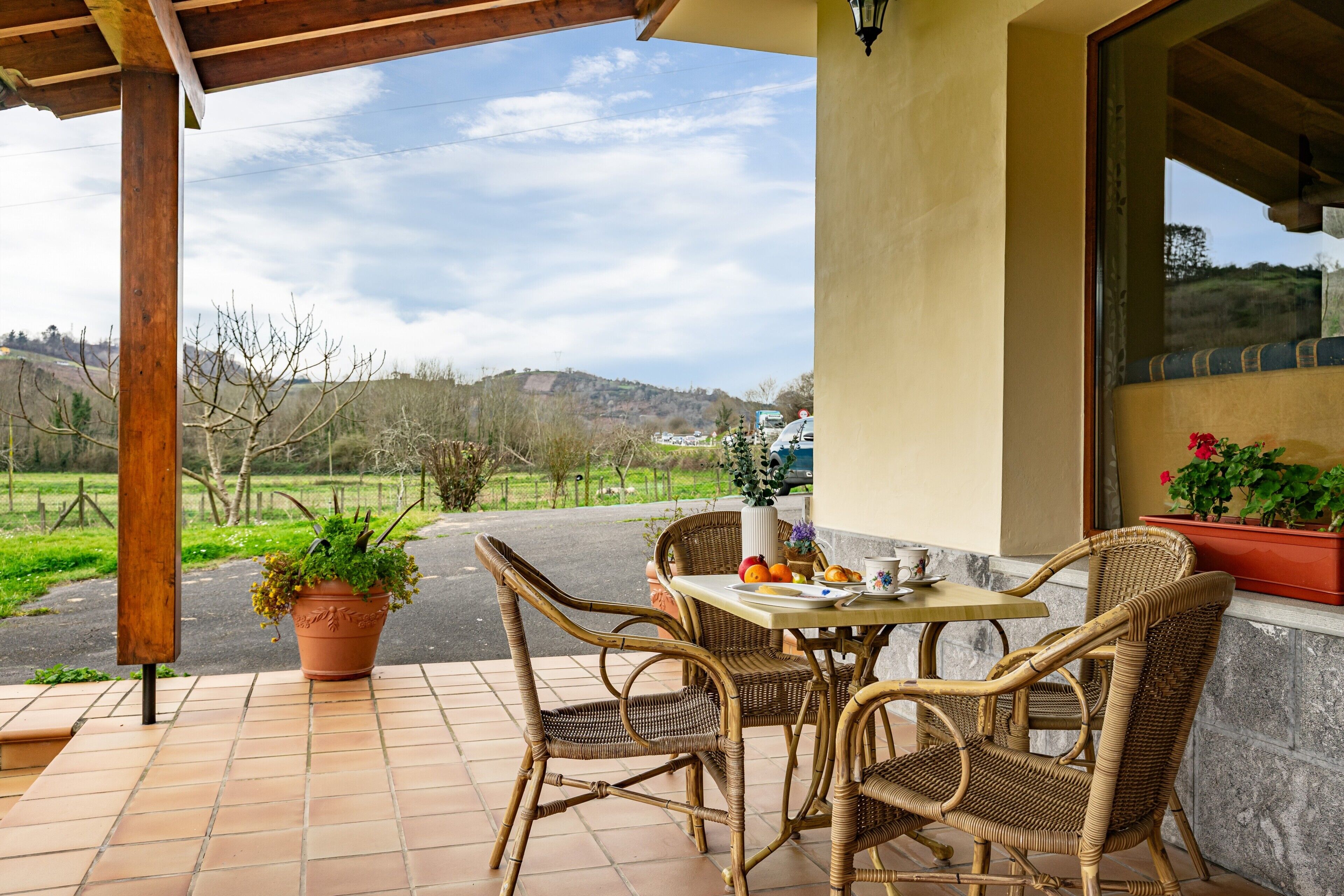 A patio with wicker furniture, a table with a vase, and a view of a hilly landscape.