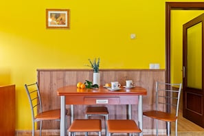 A dining area with a wooden table, four chairs, a vase with flowers, and a framed picture on the wall.