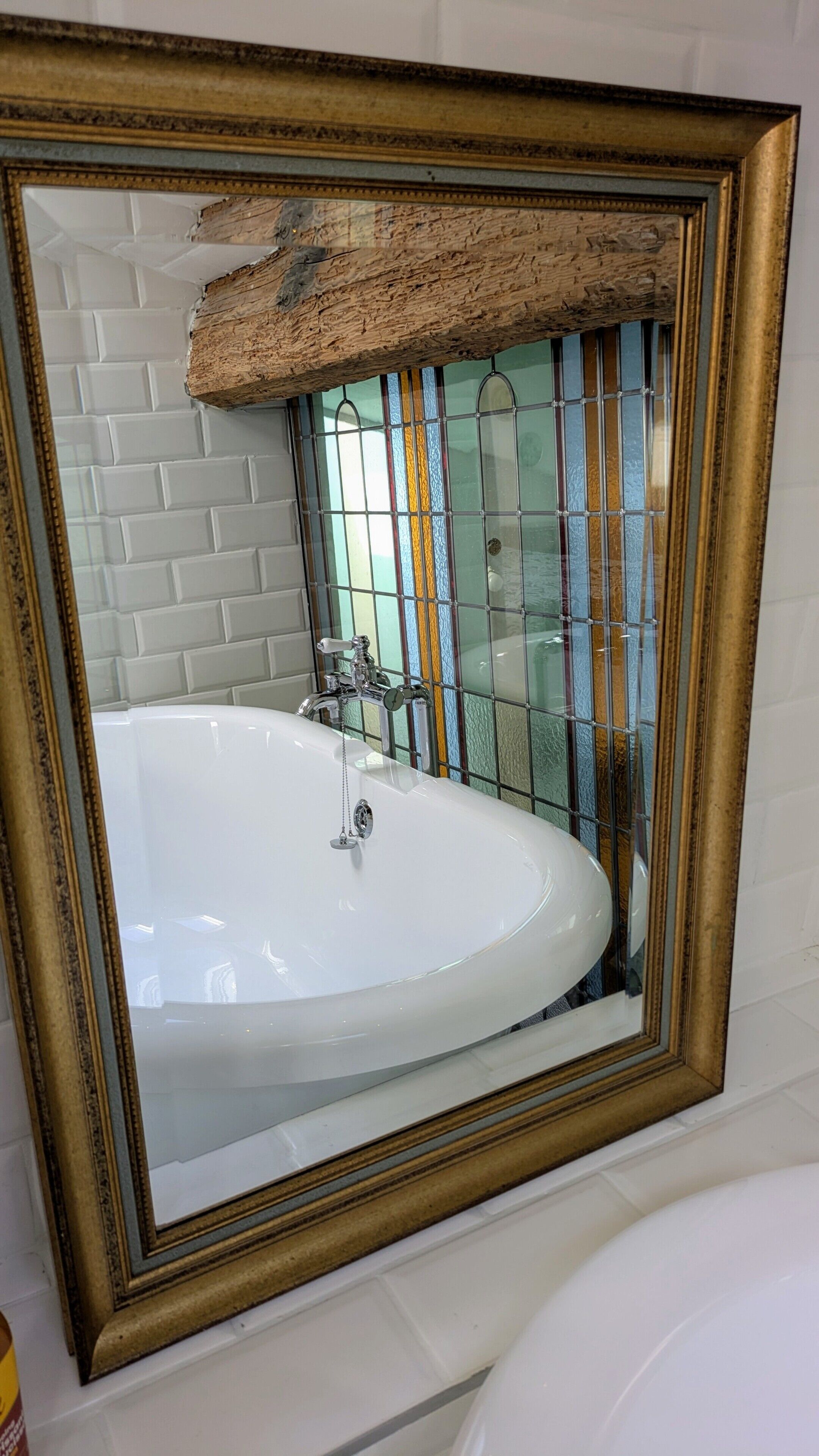 Een badkamer met een witte badkuip, een spiegel met gouden lijst en een betegelde wand.