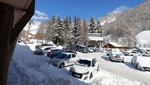Parcheggio innevato con auto e un edificio sullo sfondo.