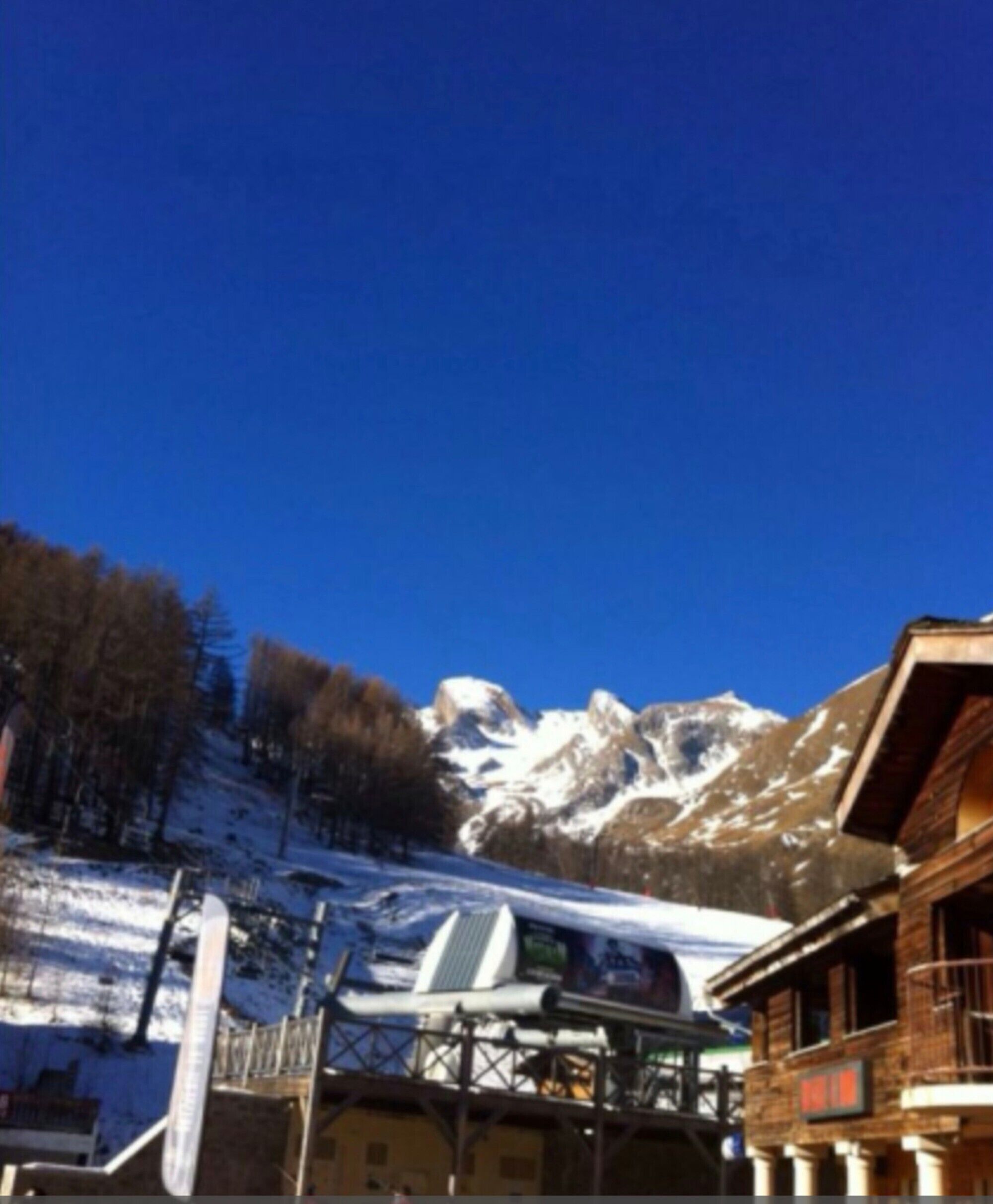 Eine Berglodge mit Seilbahn, schneebedeckten Hängen und blauem Himmel.