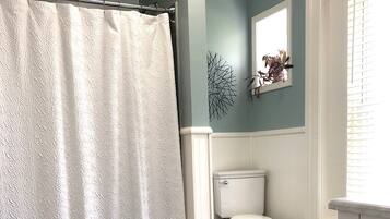 A bathroom with a white toilet, a shower curtain, and a dark wooden floor.