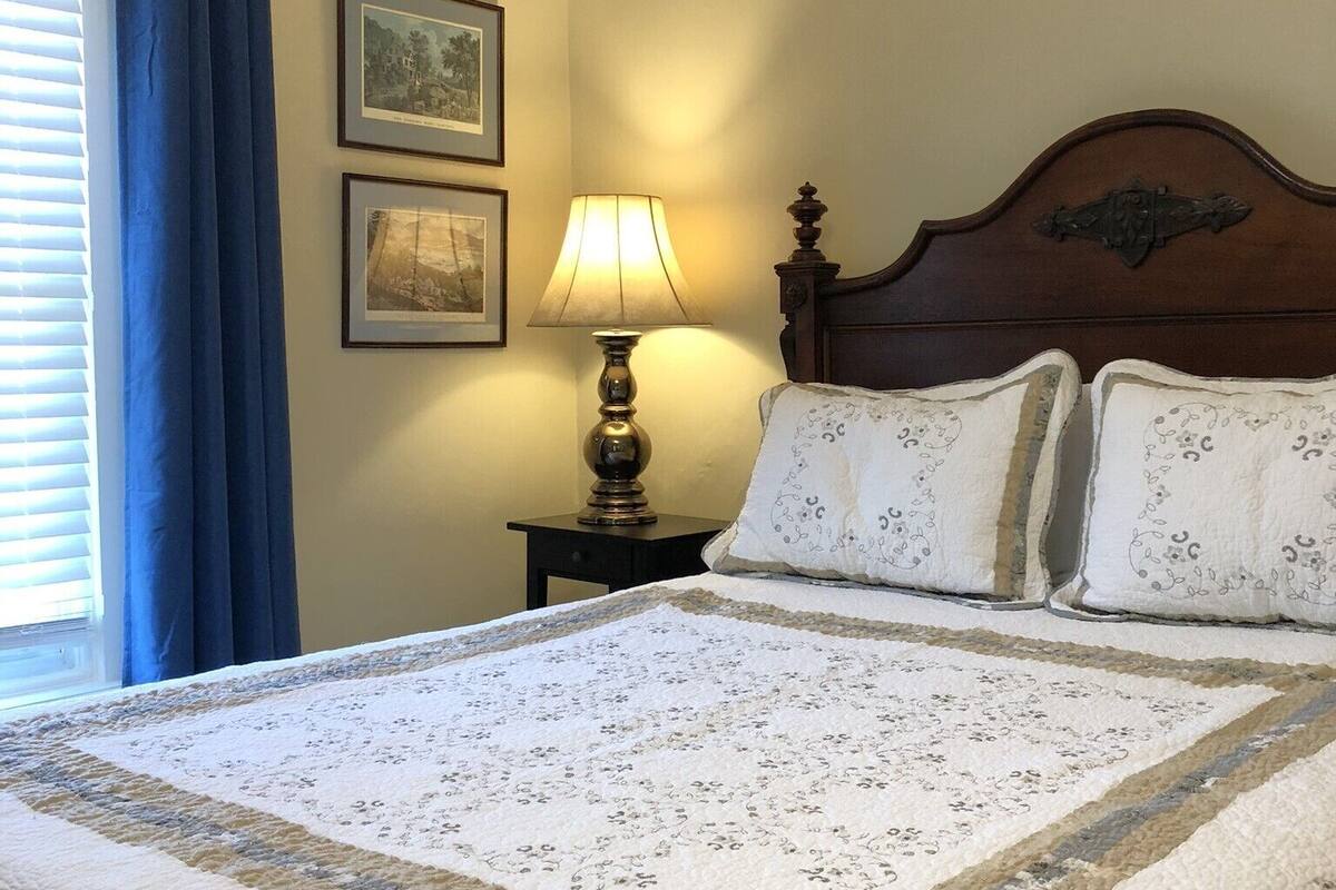Ein ordentlich bezogenes Bett mit einem blumigen Überwurf, einem Holz-Kopfteil und zwei Nachttischlampen.