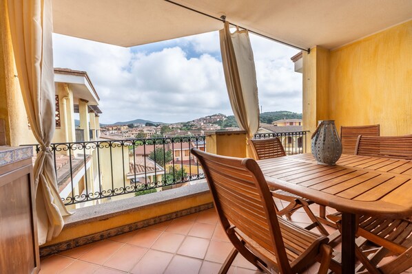 A balcony with a table and chairs, a view of a town, and a tiled floor.