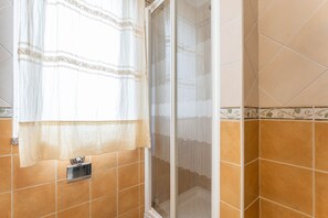 A bathroom with a shower, a towel rack, and a window with a curtain.