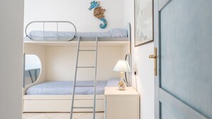 Un lit superposé avec une échelle, une table de chevet avec une lampe, une décoration représentant un hippocampe et une porte.