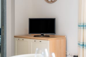 A television on a wooden cabinet, a white door, and a power outlet on the wall.