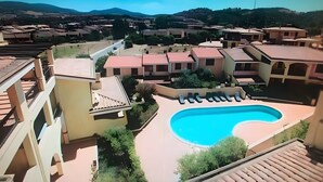 Un quartier résidentiel doté d’une piscine, de maisons aux toits rouges et d’un paysage vallonné en arrière-plan.