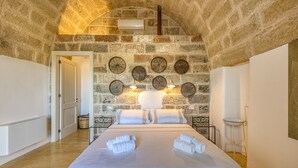 A bedroom with a stone wall, a bed with white linens, and a ceiling fan.