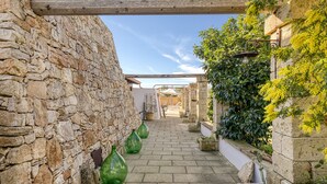 A stone-walled alley with a wooden beam overhead, potted plants, and a clear sky.