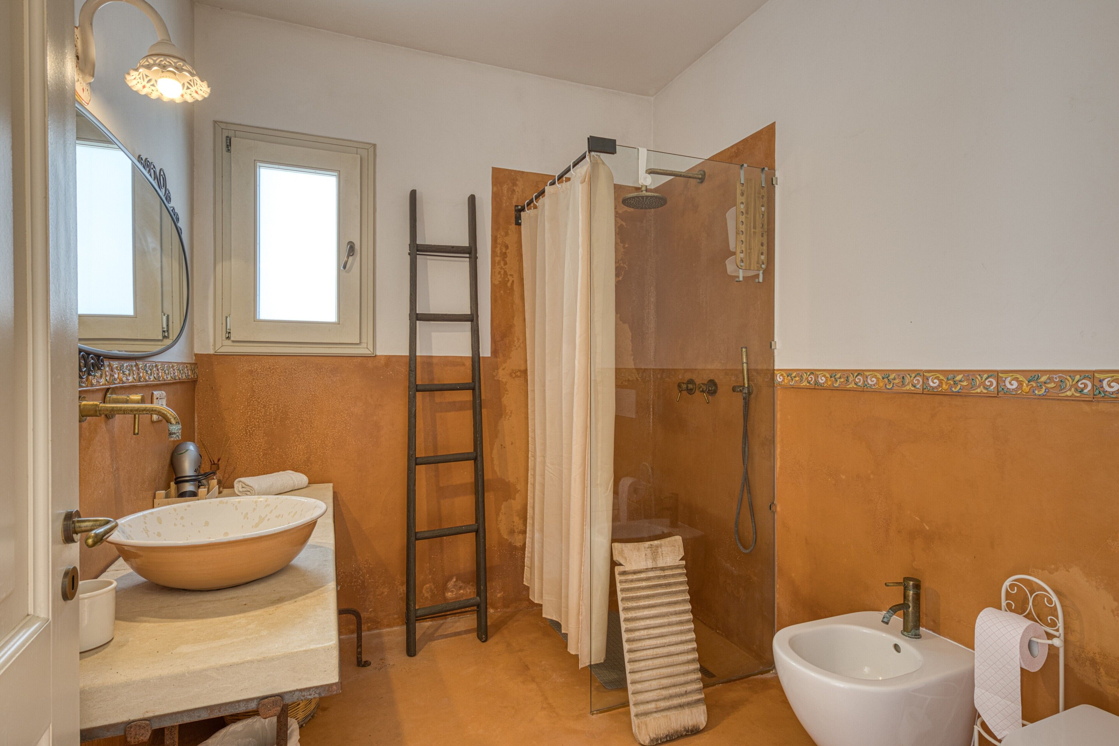 Ein Badezimmer mit einem großzügigen Waschbecken, einem separaten Standbecken, einer Dusche mit Glastür, einer Leiter und einem Handtuchhalter.
