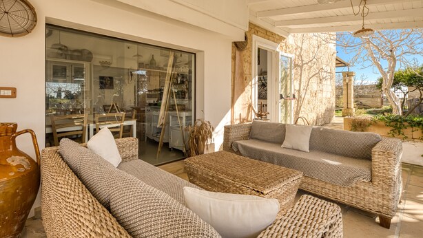 A spacious patio with wicker furniture, a large vase, and a dining area visible through glass doors.