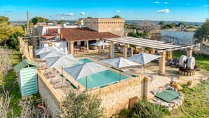 A rooftop pool area with umbrellas, lounge chairs, and a stone building with a tiled roof.