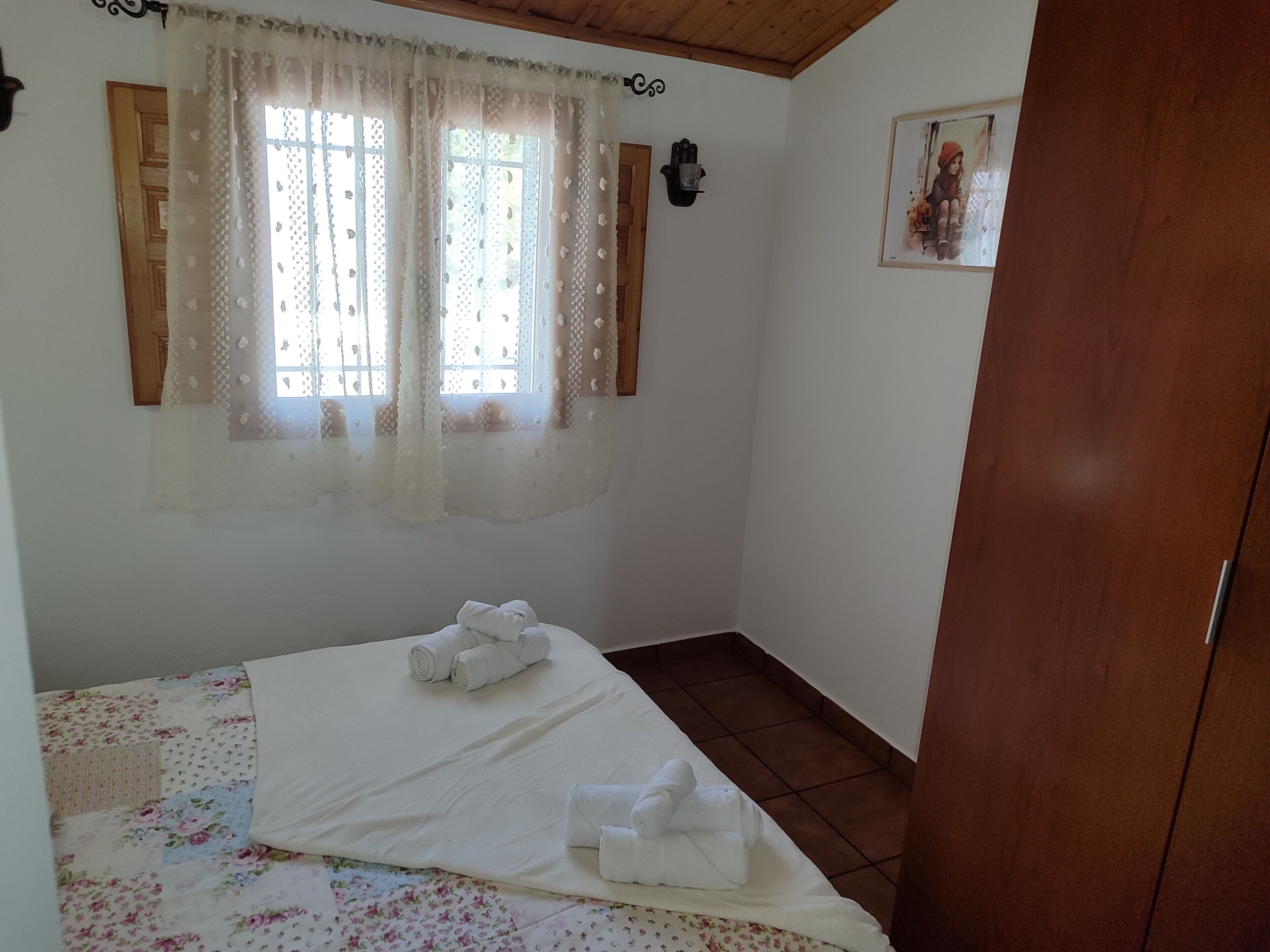 A bedroom with a bed, a window with curtains, a wooden wardrobe, and a wall-mounted picture.