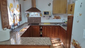 A kitchen with granite countertops, wooden cabinets, a stainless steel range hood, a microwave, and a refrigerator. - Country House 'El Serrano' with Mountain View, Wi-Fi and Air Conditioning (Murcia)