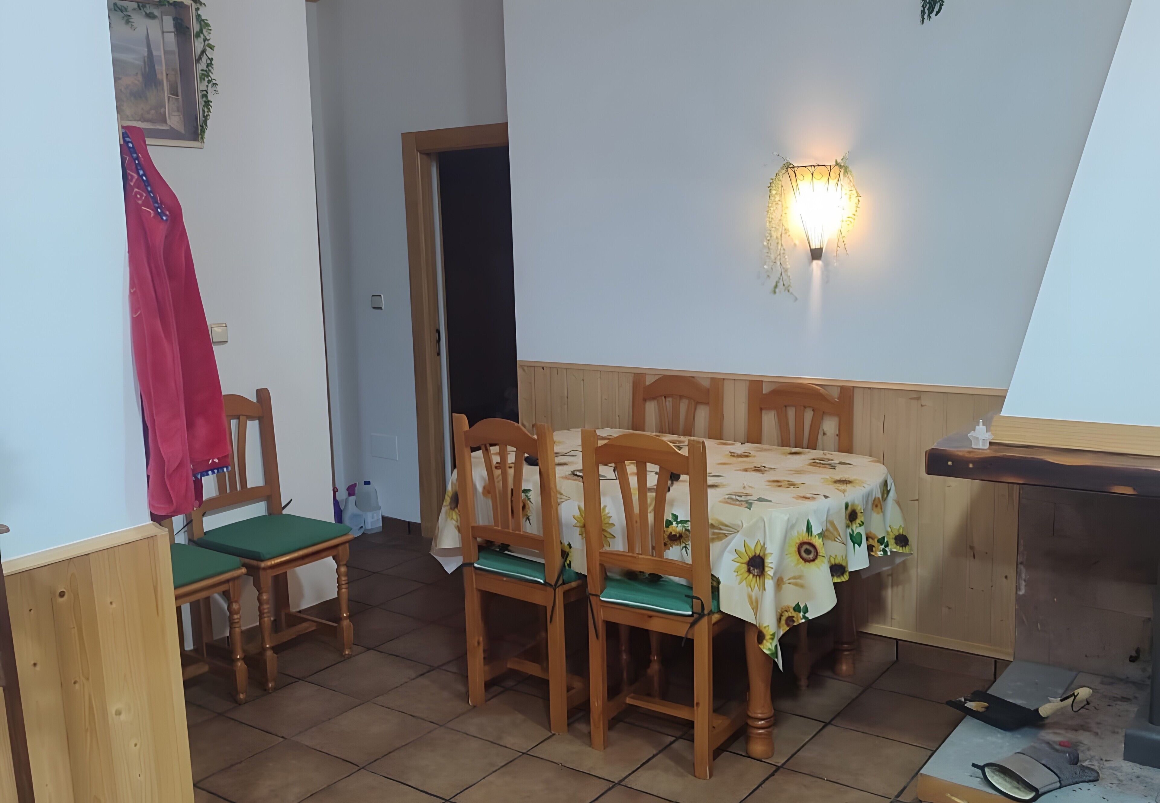 Ein Essbereich mit einem Tisch, bedeckt mit einer Sonnenblumen-Tischdecke, Holzstühle und einer wandmontierten Leuchte.