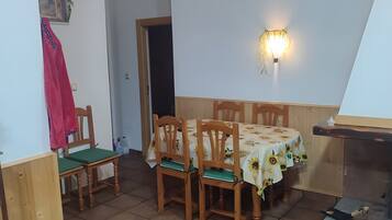 Un comedor con una mesa cubierta con mantel de girasoles, sillas de madera y una lámpara de pared.