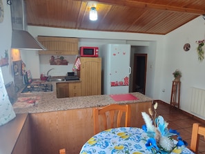 Eine Küche mit Holzausstattung, einer Mikrowelle, einem Kühlschrank, einem Gasherd und einem Essbereich mit Tisch und Stühlen.