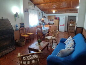Ein Wohnzimmer mit blauem Sofa, Holzstühlen, einem Kamin und einer Küche im Hintergrund.