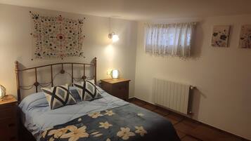 A bedroom with a bed, nightstands, a wall-mounted lamp, a radiator, and a window with curtains.
