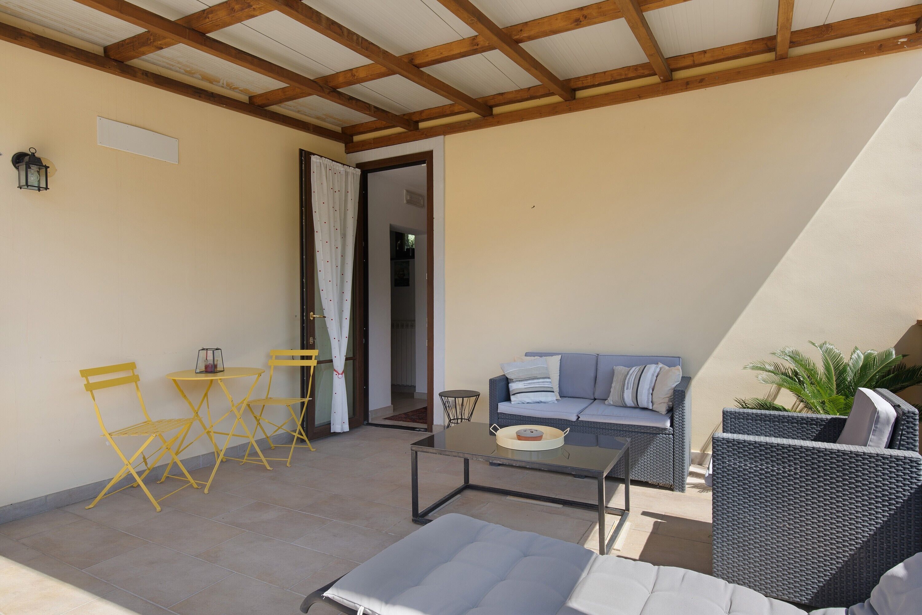 A covered patio area with a sofa, chairs, a table, and a potted plant.