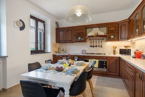Una cocina con armarios de madera, una mesa de comedor con sillas, una lámpara colgante y una ventana con cortinas.