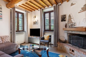 Una sala de estar con sofá, sillón, mesa de centro de vidrio, chimenea y ventanas amplias.