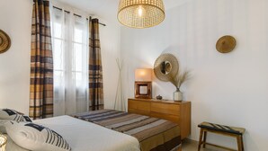 Une chambre à coucher avec un lit, des rideaux, une table de chevet, une lampe et un miroir fixé au mur.